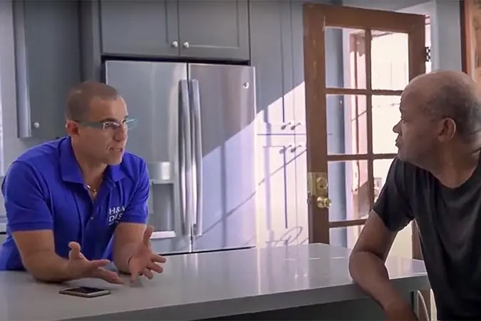 An H&A My Design team member in a company shirt sitting with a client at a kitchen counter.