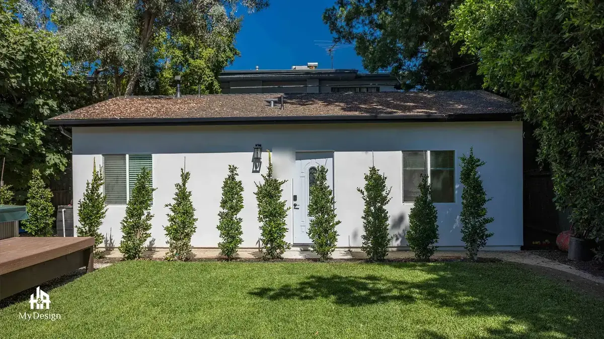 The completed detached ADU in Sherman Oaks seen whole from the garden, with a hedge screen and lawn.