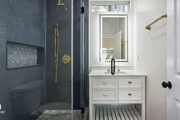 Second bathroom with navy tile, brass fittings and a lit mirror.