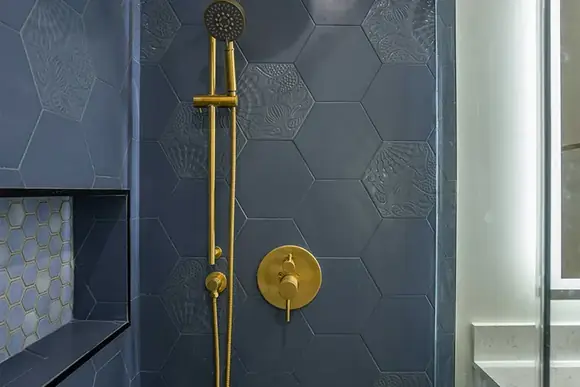 Brass shower fixtures against deep navy hexagonal tile.